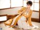 A woman in a yellow and white kimono sitting on the floor.