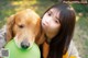 A young woman holding a green frisbee next to a dog.