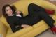 A woman in a black suit and red shoes laying on a yellow couch.