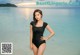 A woman in a black bathing suit standing in the ocean.